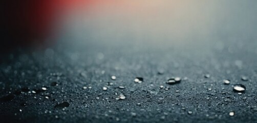  drops of water on a black surface with a red light in the backgroup of the image in the background.