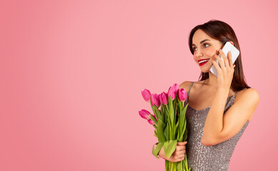 Wall Mural - Happy young woman talking on the phone, smiling brightly while holding a fresh bouquet