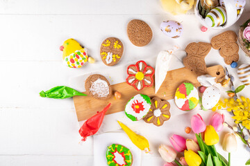 Family preparation for Easter. Holiday baking background, woman and child hands decorate homemade cookies with sugar glaze, in form of Easter symbols Easter eggs, bunny, flowers, top view copy space