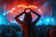 © Straxer - Woman making heart shape with hands at music event.