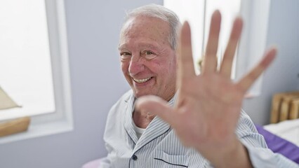 Poster - Cheerful senior man in his cozy home, donned in pyjamas, sitting on a bed in his room, raising his hand showing the number five with his fingers, all with a bright, contagious smile.