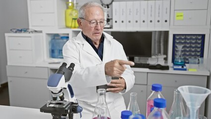 Poster - Steely-eyed senior man, a seasoned scientist standing firm in the bustling lab, pointing assertively at a touchpad. amid glowing test tubes and whirring computers, he's immersed in serious research.