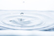 Captivating water droplet creates intriguing shapes, generating motion and splashes against a pristine white backdrop. Ideal for banners promoting freshness or hydration.