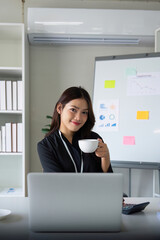 Young businesswoman asian happy during a coffee break sitting at her desk in the office