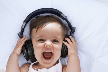 Baby, headphones and music in portrait and singing, streaming radio and podcast on bed at home. Girl, relax and hearing audio for child development or learning, toddler and fun playlist for kid