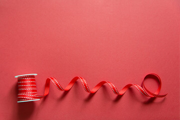 Poster - Red narrow festive ribbon on reel on a red plain paper background, top view. Blank holiday empty card. Women's, Birthday, Mother's and Valentine's Day