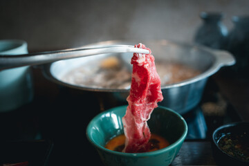 Wall Mural - Hand use tongs with raw beef dip in raw egg, shabu shabu Japanese food style