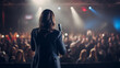Rear view of female motivational speaker standing on stage in front of audience in conference or business event