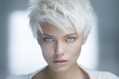 © Fantasy22 - Close-up portrait of a very beautiful young woman with light blue gray eyes and short white blonde hair, wearing a white top - isolated, blue background