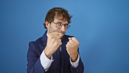 Poster - Fired up young man in business suit ready to fight his problems, fist poised in defense against isolated blue backdrop