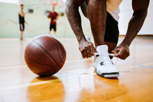 Young man tying sneakers next to basketball in gym
