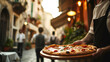 Idea for a restaurant menu, waiter serving pizza on a wooden tray in a cafe on a street in old Rome, selective focus on pizza, lunch concept with copy space