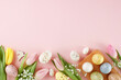 Easter-themed decor concept. Top view photo of colorful eggs, fresh flowers, easter bunnies on pastel pink background with advert area