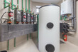 © alhim - A modern boiler room of a country house with a white water tank and a heating system with pipes and other equipment.