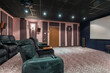Private home theater with pink and lilac decor, wide screen and soft gray armchairs.