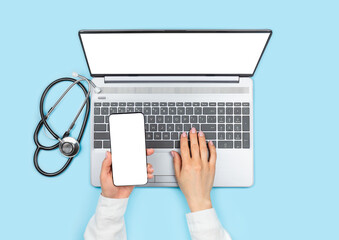 Wall Mural - Female doctor's hands holding smartphone with blank screen and using laptop with empty monitor on blue background. Telemedicine concept