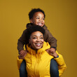 Black mother giving a piggyback to her son on a yellow background.