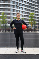 Wall Mural - Athletic woman in sportswear exercises outdoors with ball, embodying a fit and healthy lifestyle in an urban park.