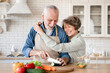 © InsideCreativeHouse - Cheerful old senior couple grandparents spouses hugging embracing cuddling while helping prepare cook romantic dinner lunch at home kitchen