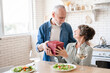 Receiving gifts - love language. Old senior husband giving present gift box to his wife while having romantic dinner date, celebrating anniversary Valentine`s Day together