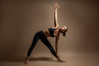 A young slim attractive girl demonstrates yoga poses in the studio on a beige background.