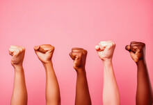 Women Rising Fists On Pink Background. Only Hands. The Picture Illustrates The Equality Of Women In Different Races.