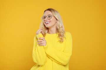 Sticker - Happy woman in stylish warm sweater and eyeglasses on orange background