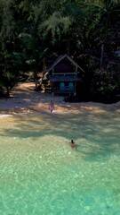 Wall Mural - Koh Wai Island Trat Thailand, wooden bamboo hut bungalow on the beach and a young couple of men and women relaxing on the beach swimming in the blue ocean on a tropical Island in Thailand