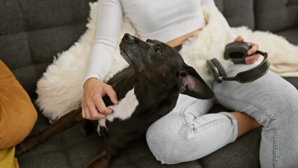 Sticker - Young caucasian woman pets her black labrador dog in a cozy living room listening to music.