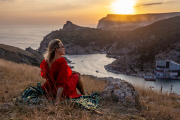 Wall Mural - Woman sunset sea mountains. Happy woman siting with her back on the sunset in nature summer posing with mountains. Woman in the mountains red dress, eco friendly, summer landscape 