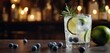  .A glass with gin, blueberry syrup and lime slices is filled halfway. The table is also topped with several blueber.