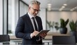 © Arceli - Happy mid aged businessman wearing suit standing in modern office using digital tablet from Generative AI