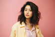 Portrait of a beautiful young asian woman in yellow raincoat on pink background