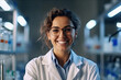 In the image, there is a smiling female scientist wearing a white lab coat and glasses, standing in a laboratory with shelves of bottles in the background.