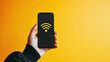 Hand holding cell phone with WIFI icon on screen on yellow background
