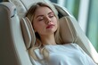 © photolas - A serene European woman enjoys a moment of relaxation while sitting in a state-of-the-art massage chair in a well-lit modern room.
