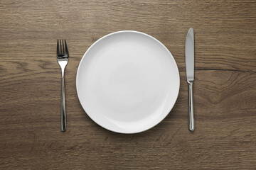 Empty plate, fork and knife on wooden table, top view