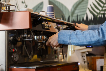 Wall Mural - Unrecognizable hands of Asian barista female making hot coffee from professional machine standing behind cafe shop counter bar, young waitress worker wearing apron working in cozy small restaurant