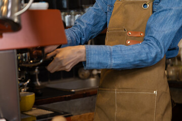 Wall Mural - Unrecognizable hands of Asian barista female making hot coffee from professional machine standing behind cafe shop counter bar, young waitress worker wearing apron working in cozy small restaurant