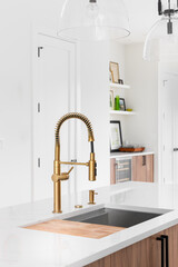 Wall Mural - A gold kitchen faucet detail with a white marble countertop, cutting board on sink, and blurred decorations in the background.