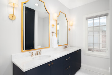 Wall Mural - A bathroom with a blue cabinet, white marble countertop, and gold light fixtures and mirrors.