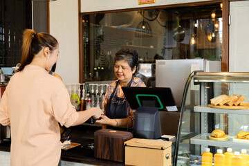 Wall Mural - Asian waitress barista worker accepts credit card cashless payments from customer female in cafe restaurant, happy woman open bakery coffee shop, small business entrepreneur start-up lifestyle