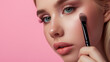 Close-up of the face of a young blond woman applying blush or powder to her face with a brush. Beauty shot.