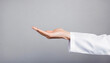 © Loliruri - Half cropped close up of hand with white coat sleeve holding invisible object on gray background with copy space