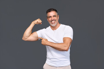 Happy fit sporty older man coach, middle aged sportsman athlete personal trainer wearing white t-shirt showing muscles pointing at biceps stands isolated on gray background advertising gym membership.