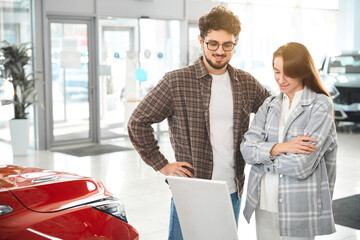 Wall Mural - Couple buying car in salon standing at the dealership choosing the car to buy