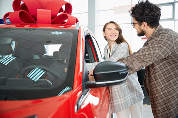 Wall Mural - Cheerful man and woman in car dealership and choosing color of the future car