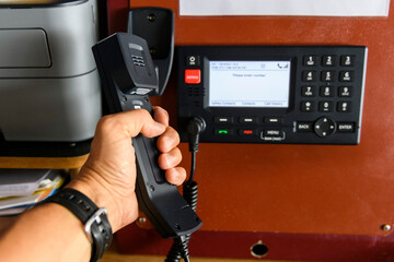 Navigational control panel and VHF radio with hand. Radio communication at sea. Working on the ship's bridge.