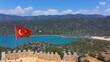 Simena castle in Kalekoy and Turkish flag waving in hot summer breeze. Amphitheater with 7 rows of seats carved into rock in the castle, can host 300 people, smallest theater among the Lycian cities