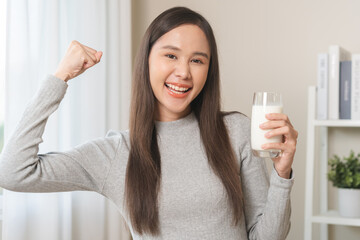 Wall Mural - Health care, smile asian young woman, girl gesture strong holding a glass of fresh, dairy soy milk to drink for calcium, vitamin wholesome good nutrition in morning at home, product of healthy people.